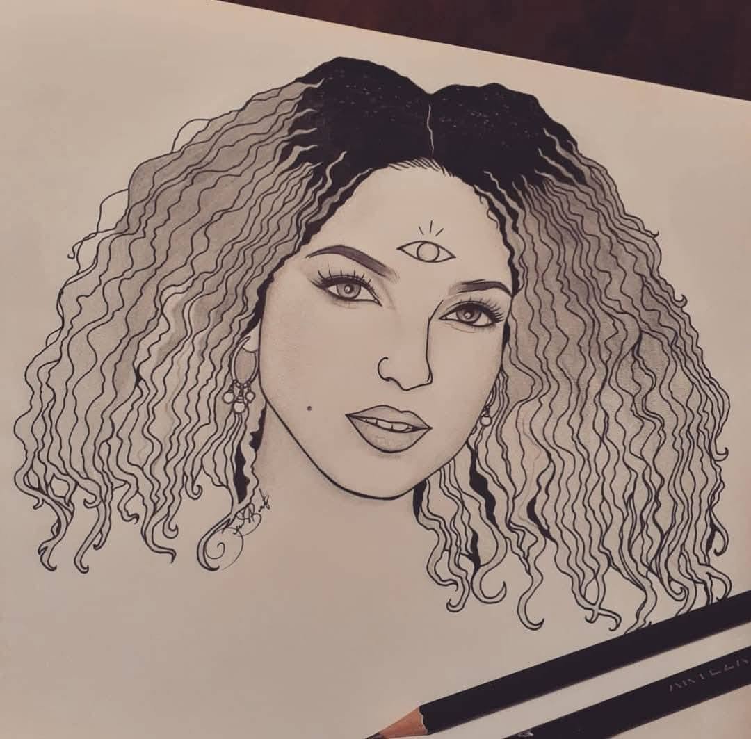 Ink portrait of a woman with a full crown of natural curls and a small third eye, the artist's pen resting at the edge of the page