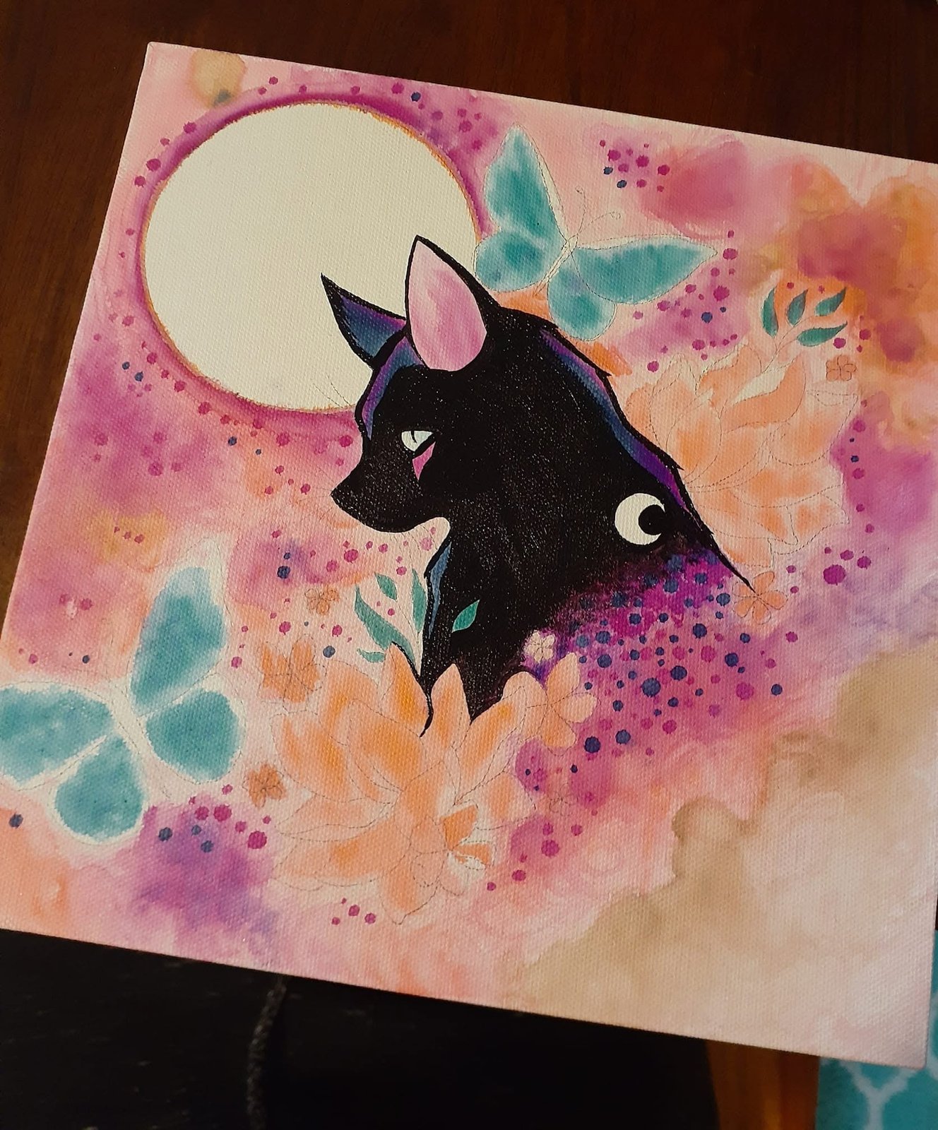 Watercolor of a black cat beneath a full moon, teal butterflies and splashes of pink and orange around it